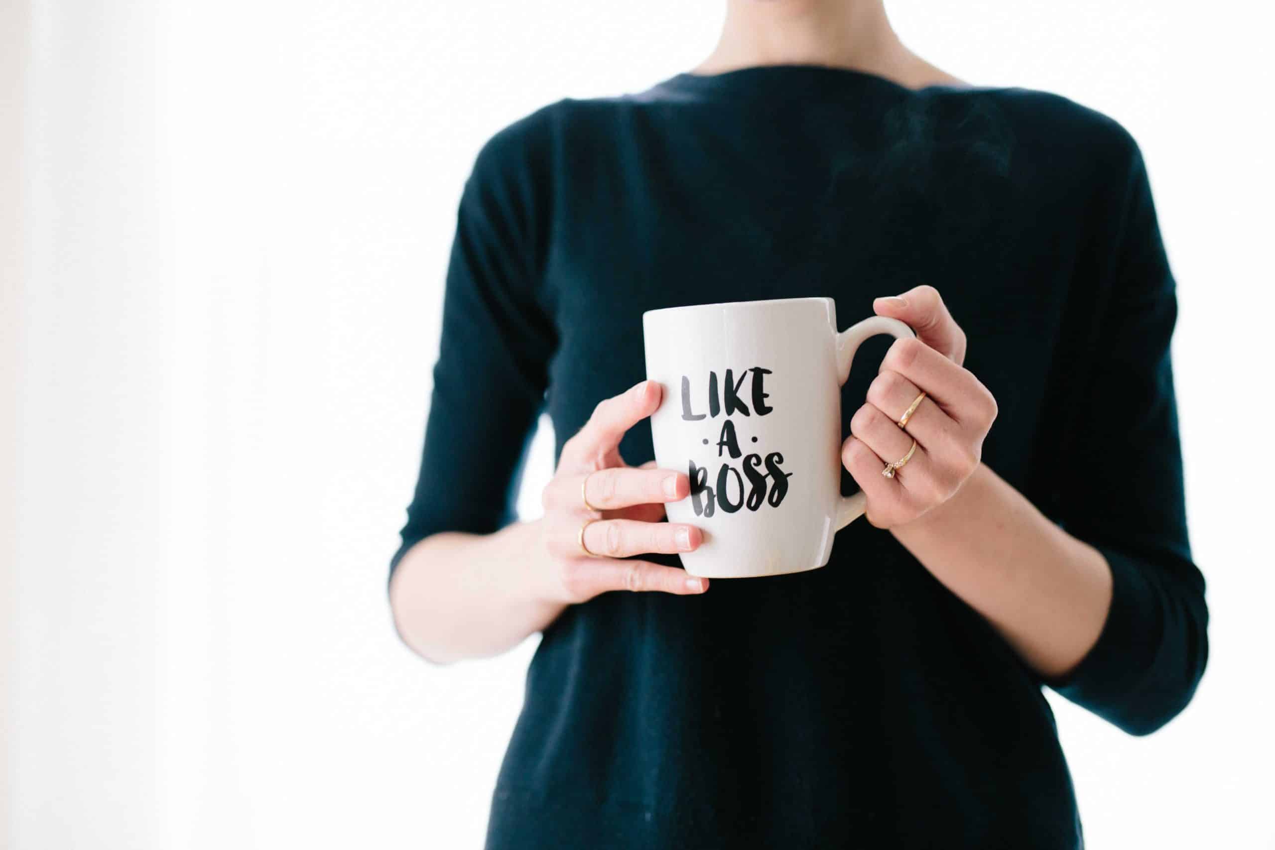 A woman dressed in professional clothes holds a mug that reads 'Like A Boss'